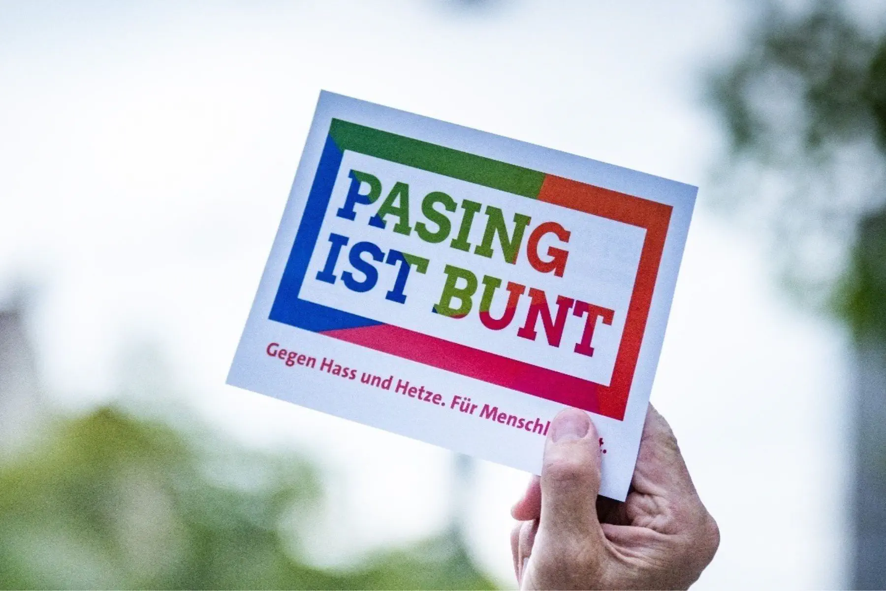 Eine Hand hält ein Schild mit der Aufschrift "Pasing ist bunt" in die Höhe